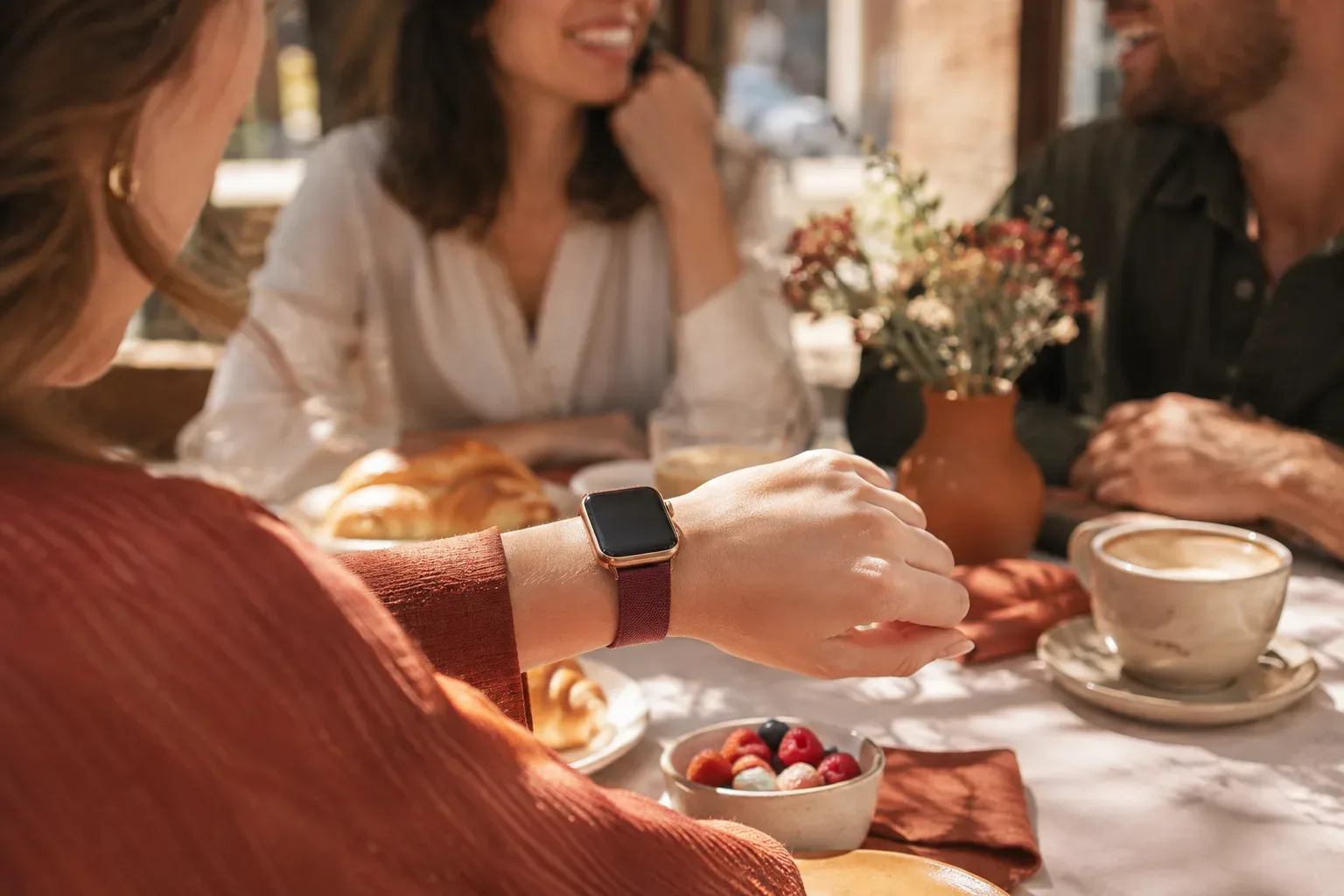 Aranyszínű Apple Watch bordó szíjjal egy baráti brunch találkozón.